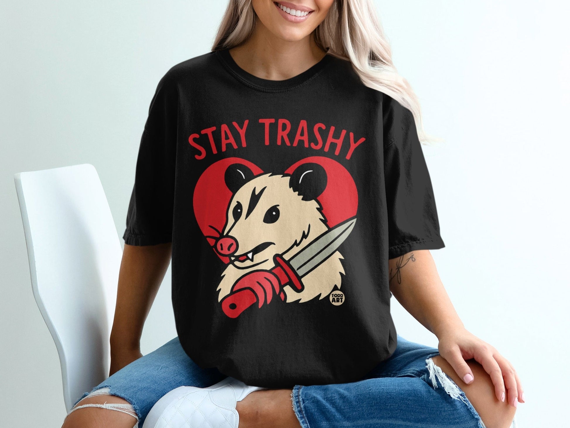 Black t-shirt with "Stay Trashy" and a possum holding a knife over a red heart.