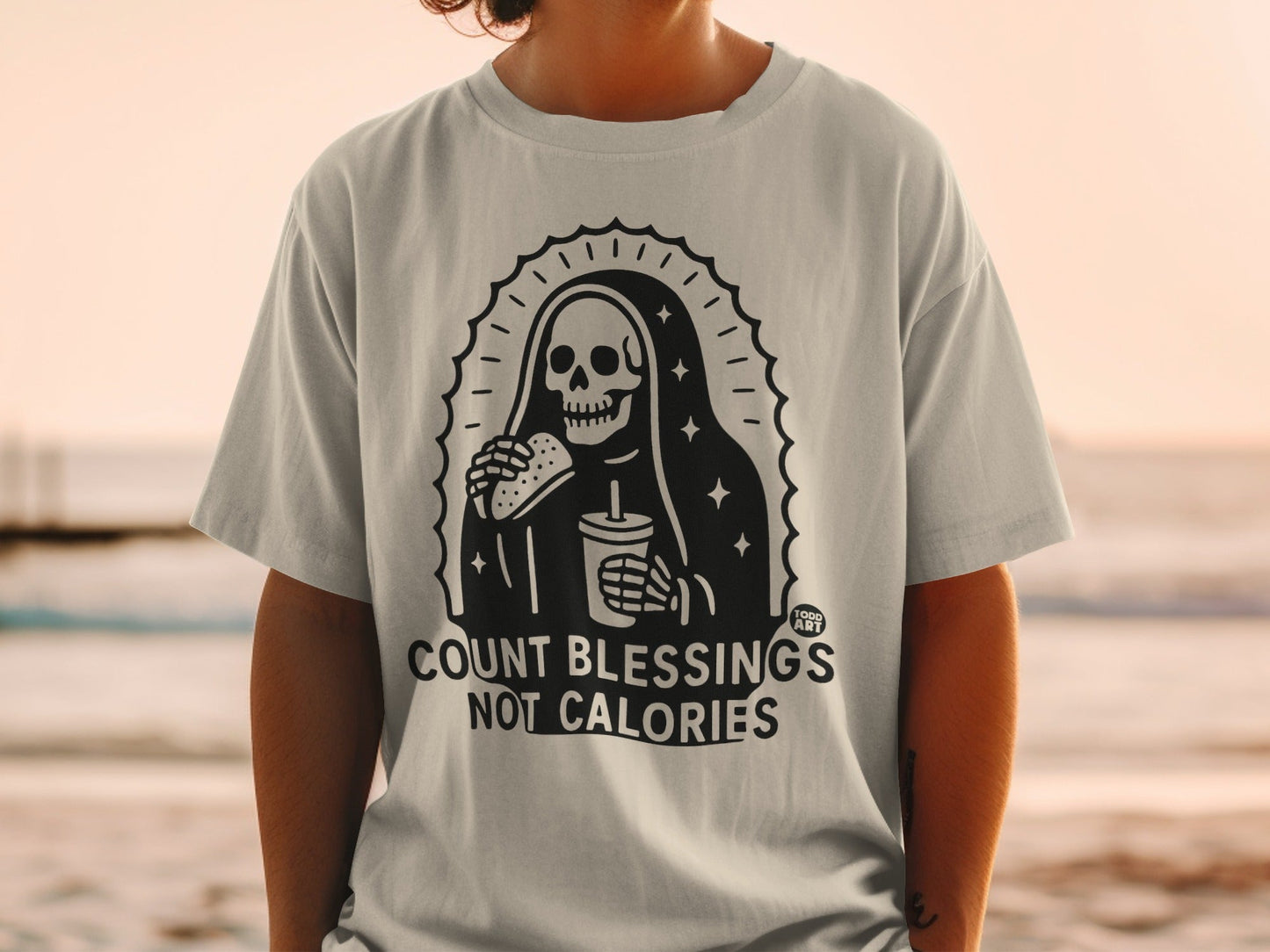 T-shirt with skeleton Grim Reaper eating burger and drinking soda, "Count Blessings Not Calories" text.