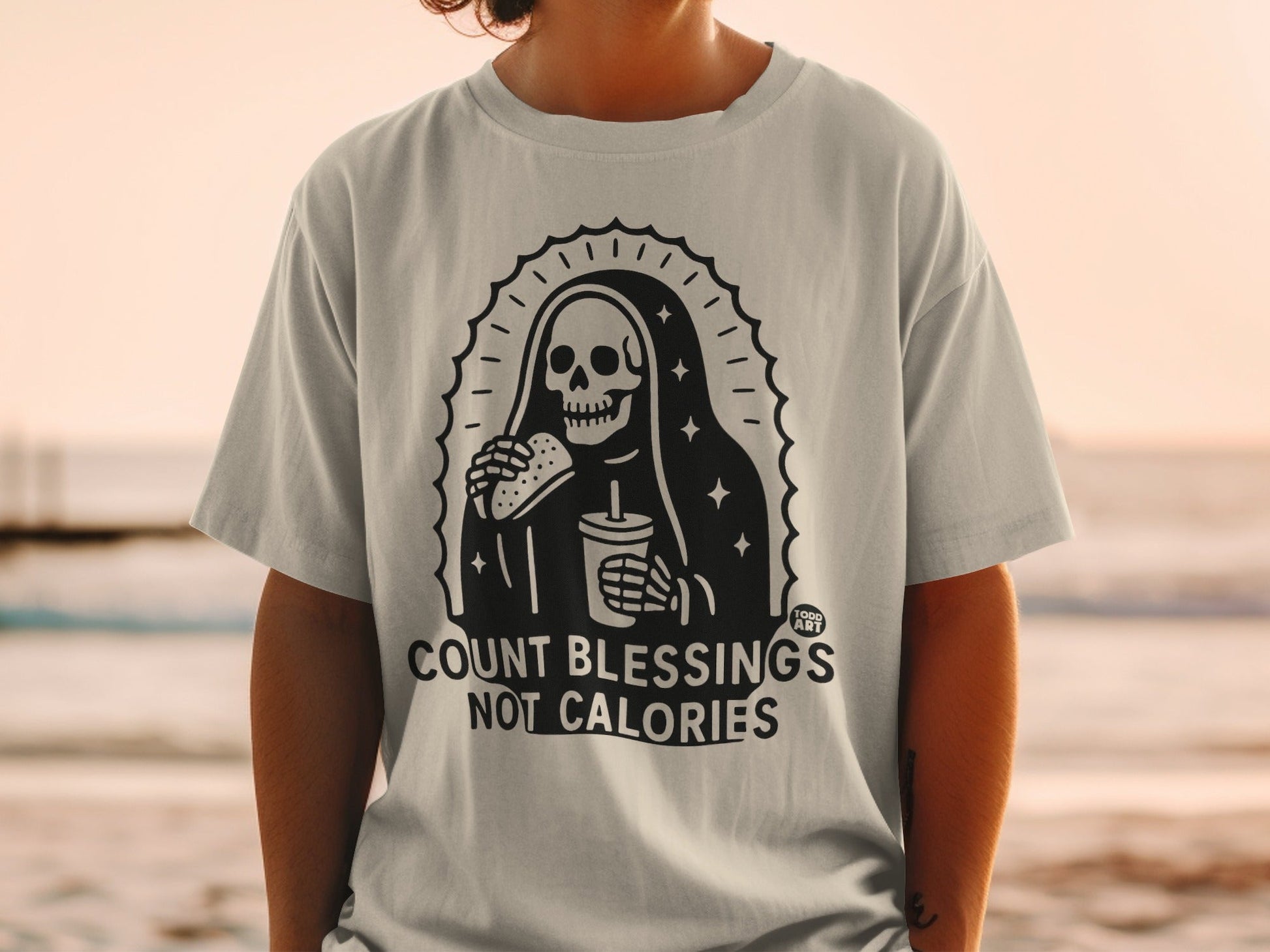 T-shirt with skeleton Grim Reaper eating burger and drinking soda, "Count Blessings Not Calories" text.