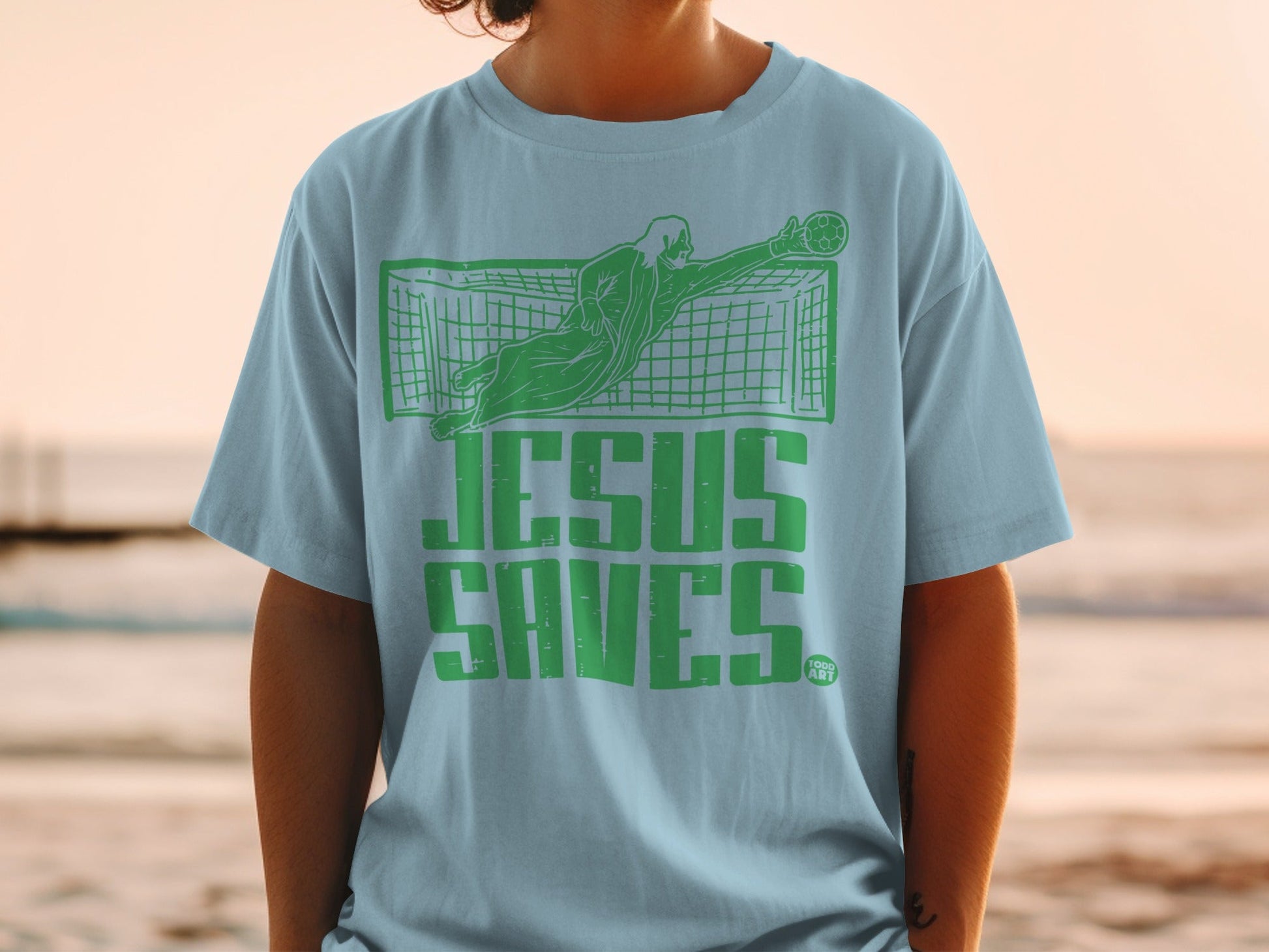 Light blue t-shirt with green "Jesus Saves" text and soccer goalie graphic.