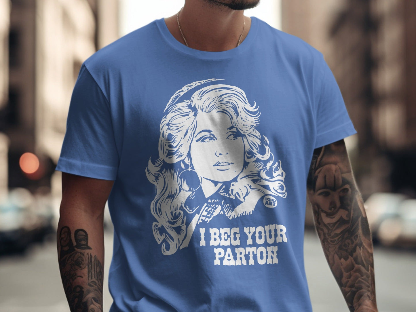 Blue t-shirt with white graphic of Dolly Parton and "I BEG YOUR PARTON" text.