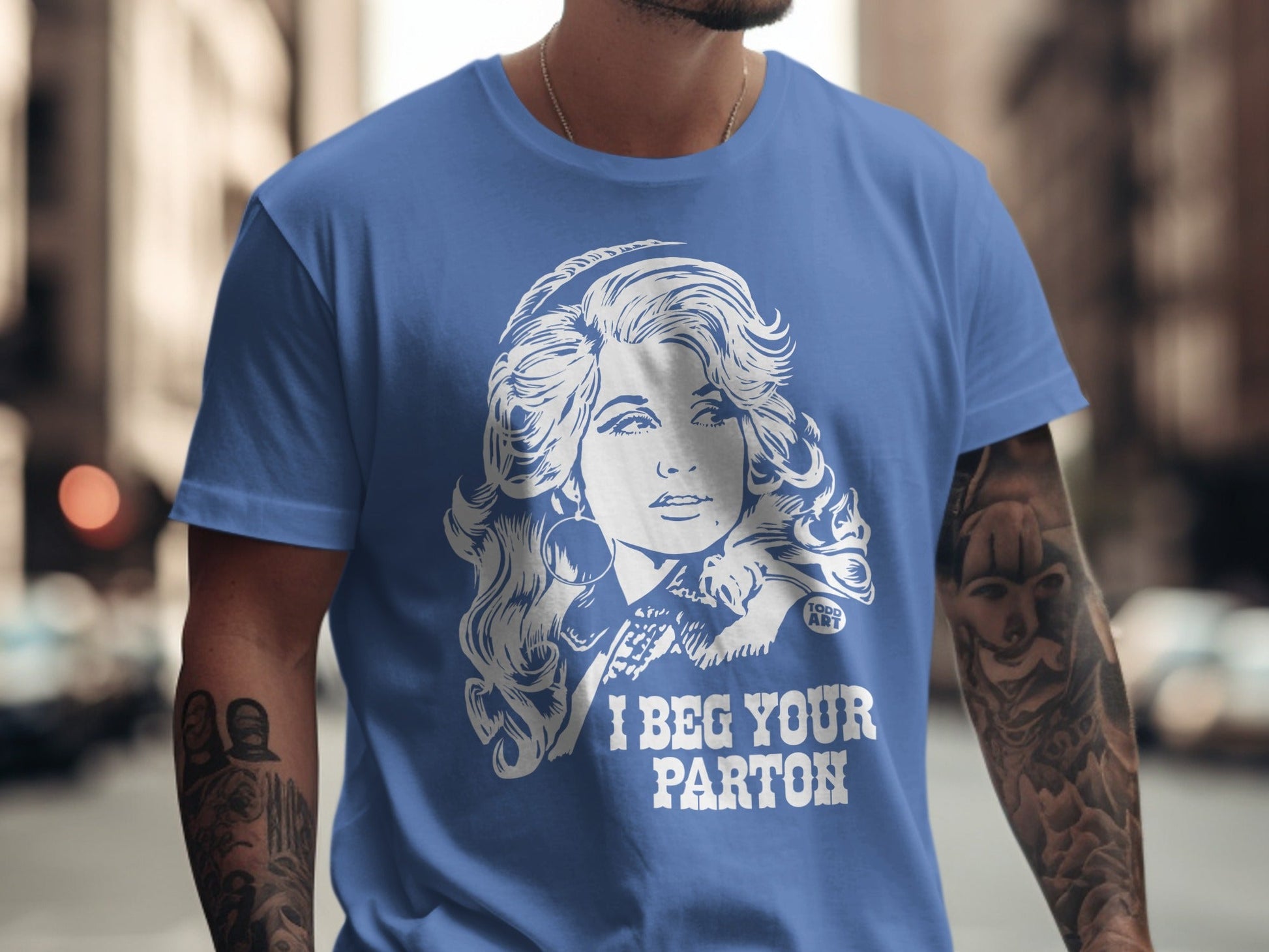 Blue t-shirt with white graphic of Dolly Parton and "I BEG YOUR PARTON" text.