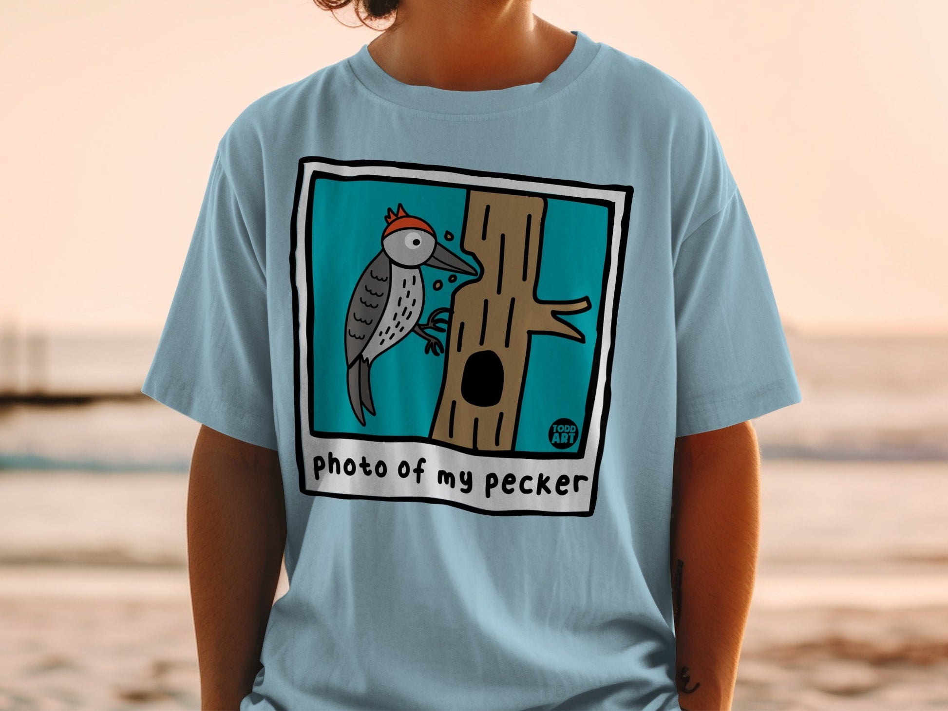 Light blue t-shirt with a cartoon woodpecker on a tree, saying "photo of my pecker".