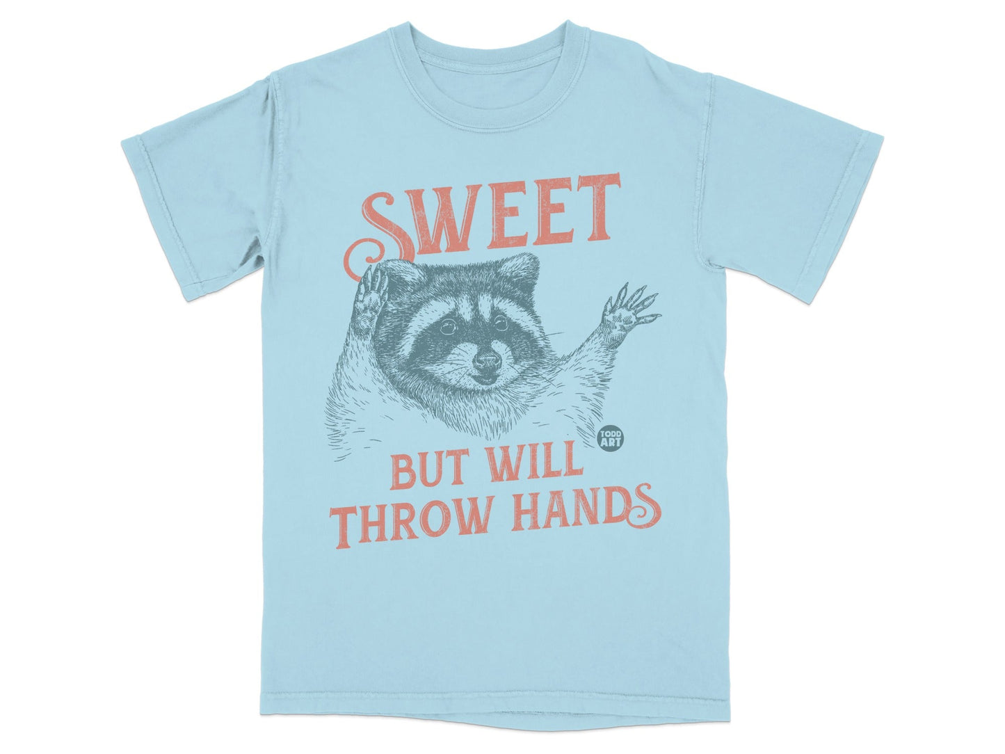 Light blue t-shirt with raccoon illustration and "SWEET BUT WILL THROW HANDS" text.