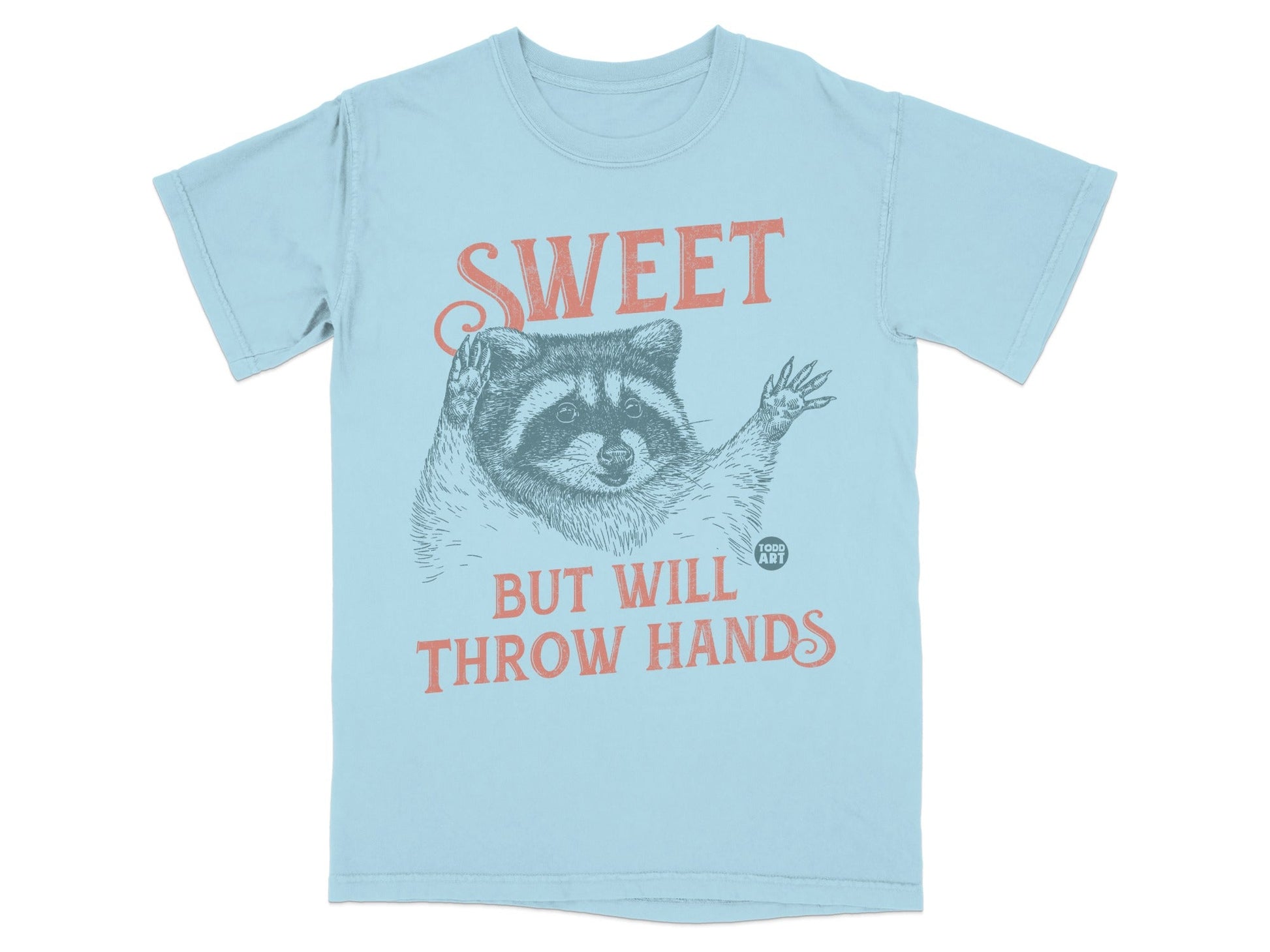Light blue t-shirt with raccoon illustration and "SWEET BUT WILL THROW HANDS" text.