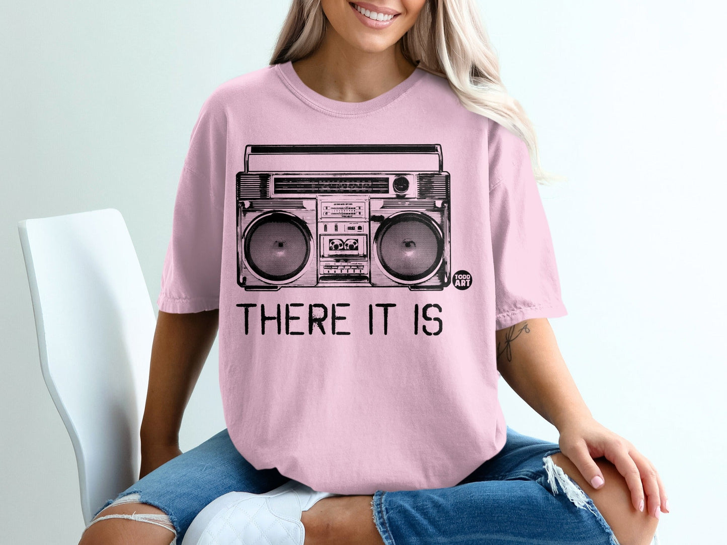 Pink t-shirt with black illustration of a boombox and text "THERE IT IS".