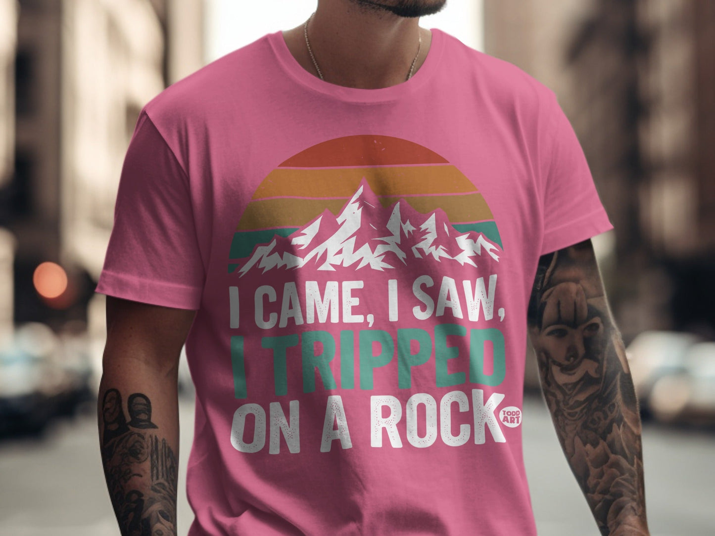 Pink t-shirt with mountains and text "I came, I saw, I tripped on a rock".
