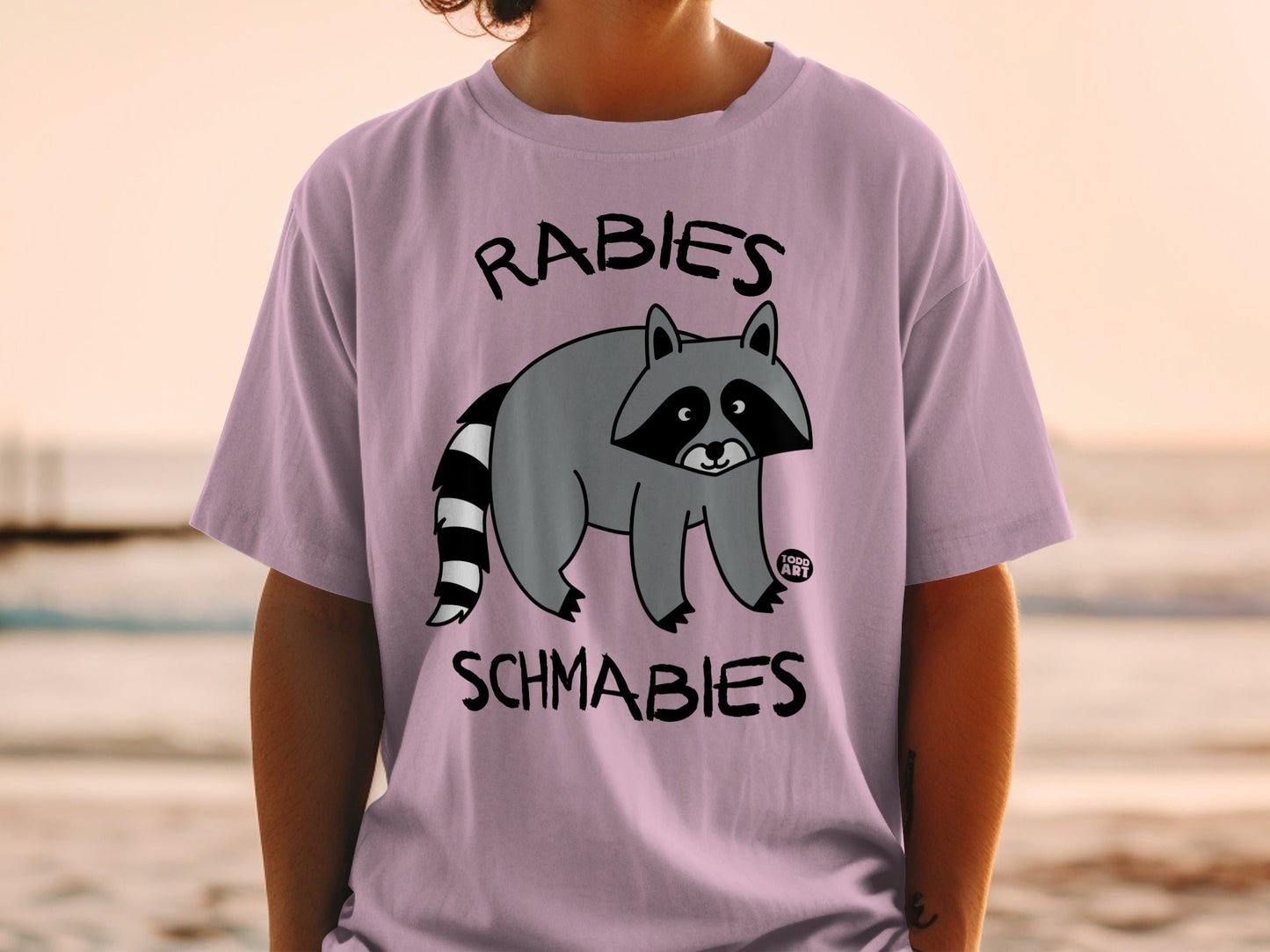 T-shirt with a cartoon raccoon and the text "Rabies Schmabies".