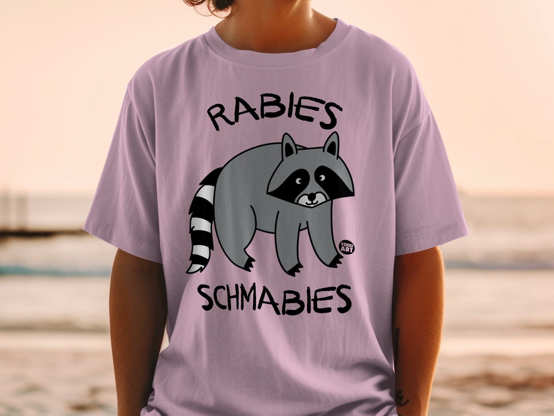 T-shirt with a cartoon raccoon and the text "Rabies Schmabies".
