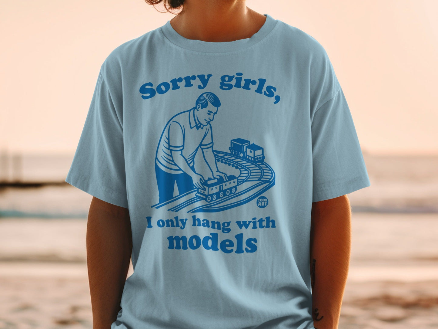 Light blue t-shirt with man playing with toy train set and text.