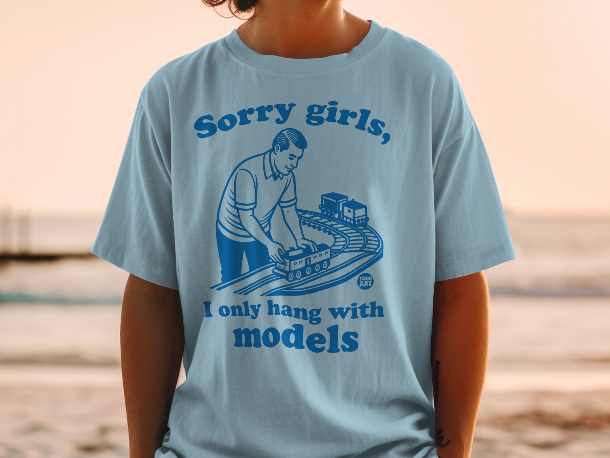 Light blue t-shirt with man playing with toy train set and text.