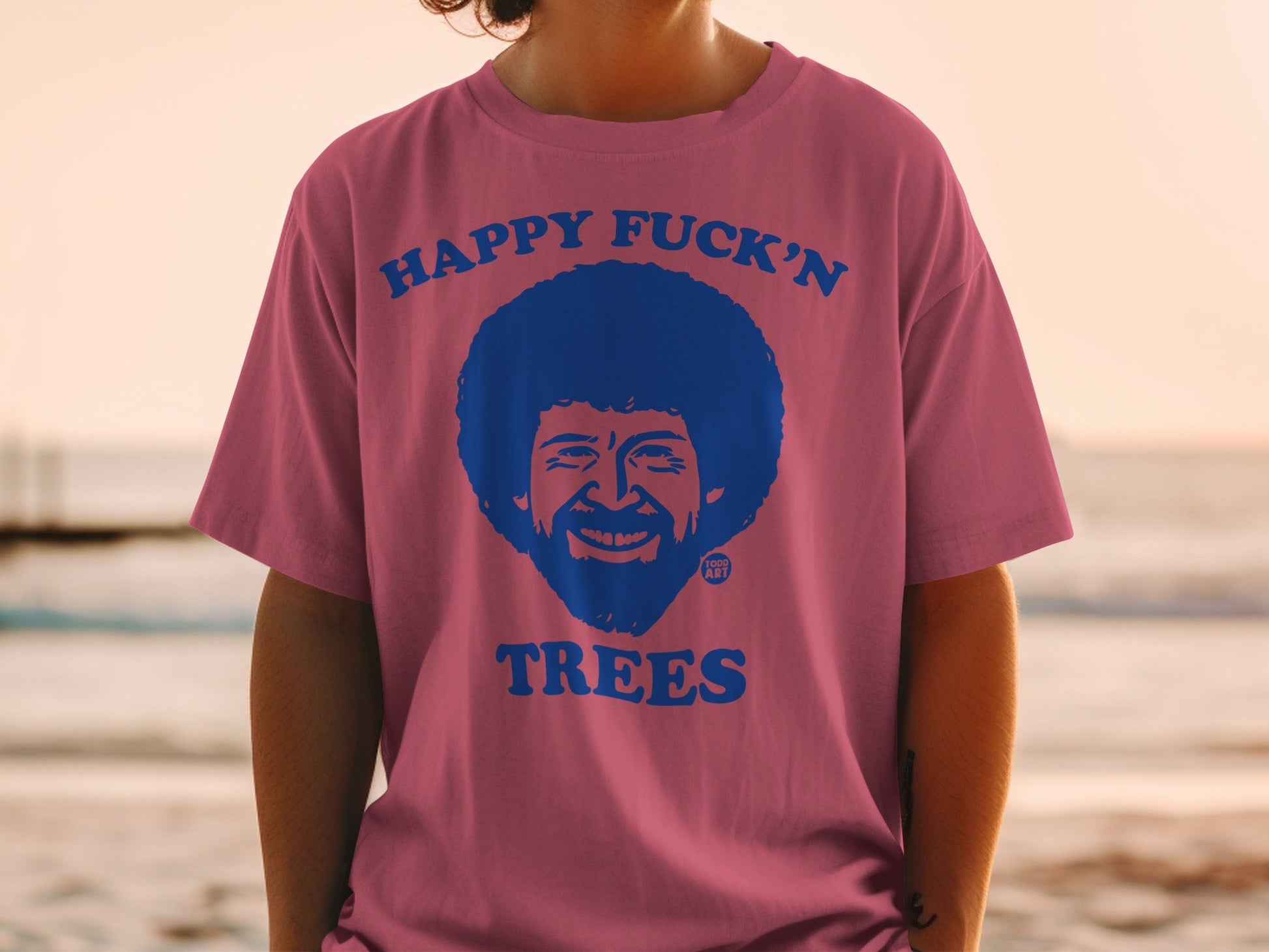 Pink t-shirt with Bob Ross graphic and text "HAPPY FUCK'N TREES".
