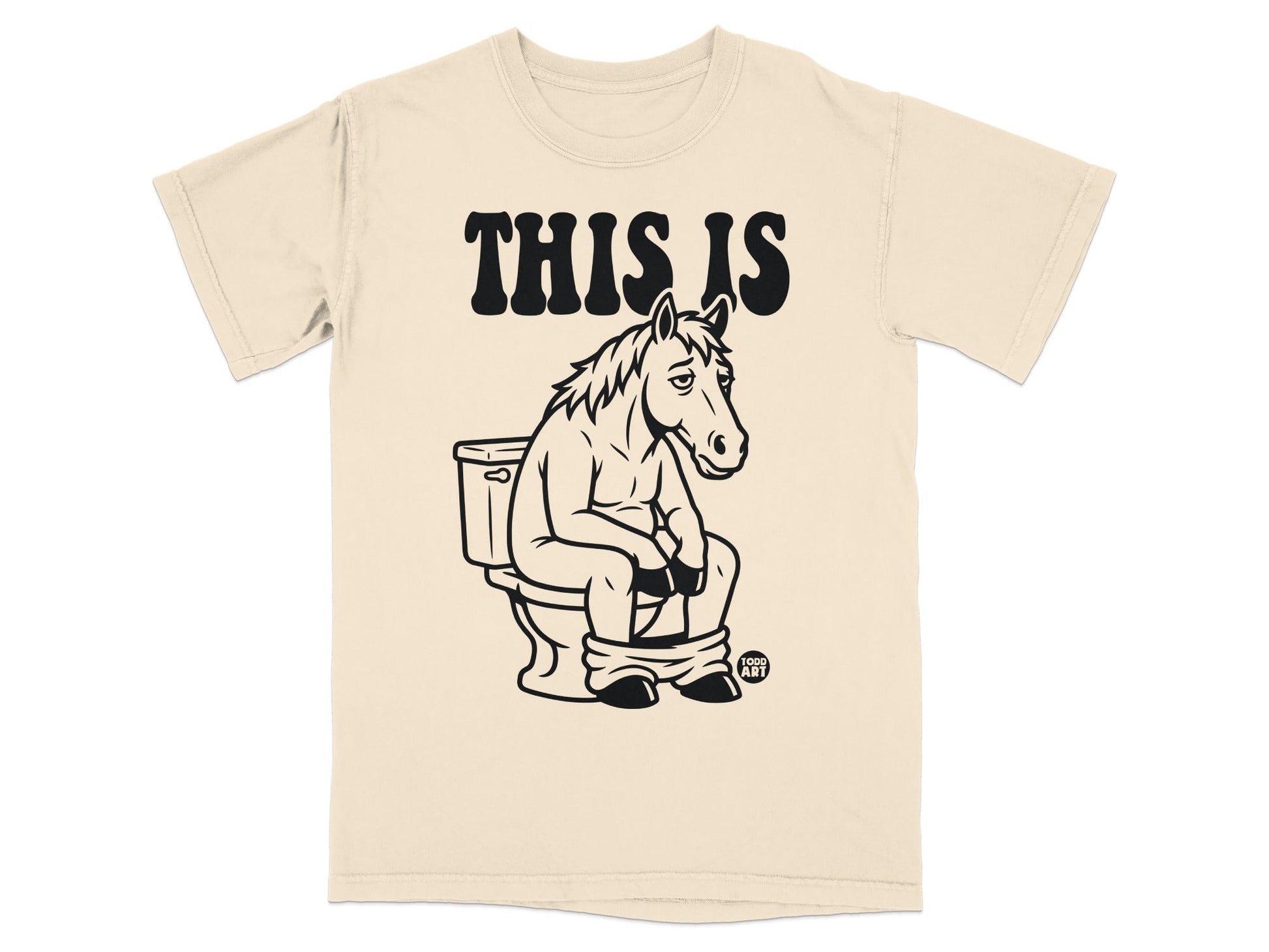 Cream t-shirt with a drawing of a horse sitting on a toilet, text above reads "THIS IS".