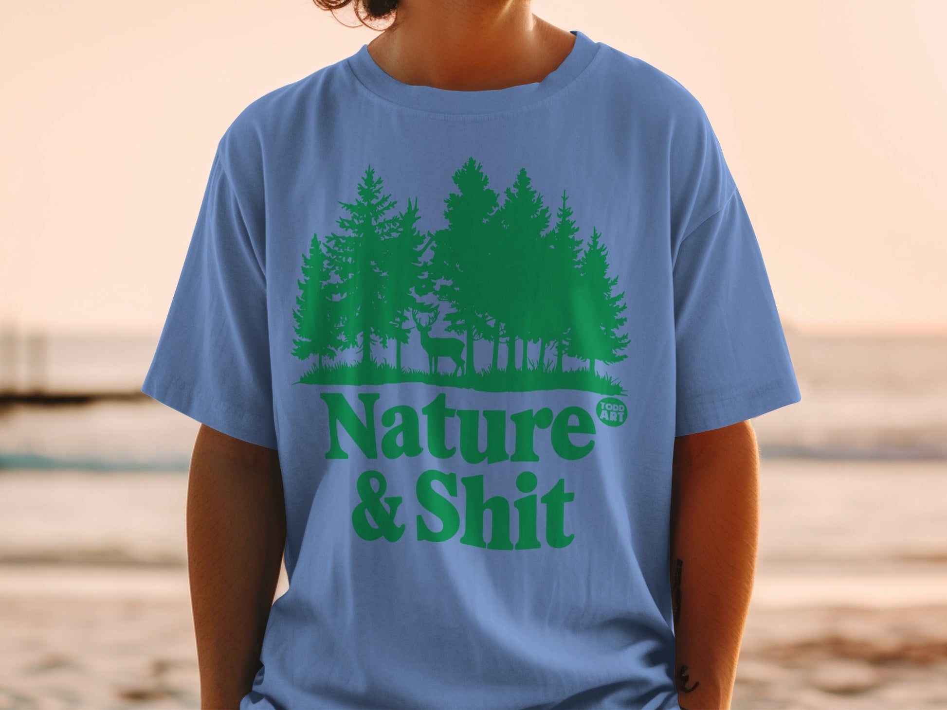 Blue t-shirt with green forest and deer graphic, text "Nature & Shit".