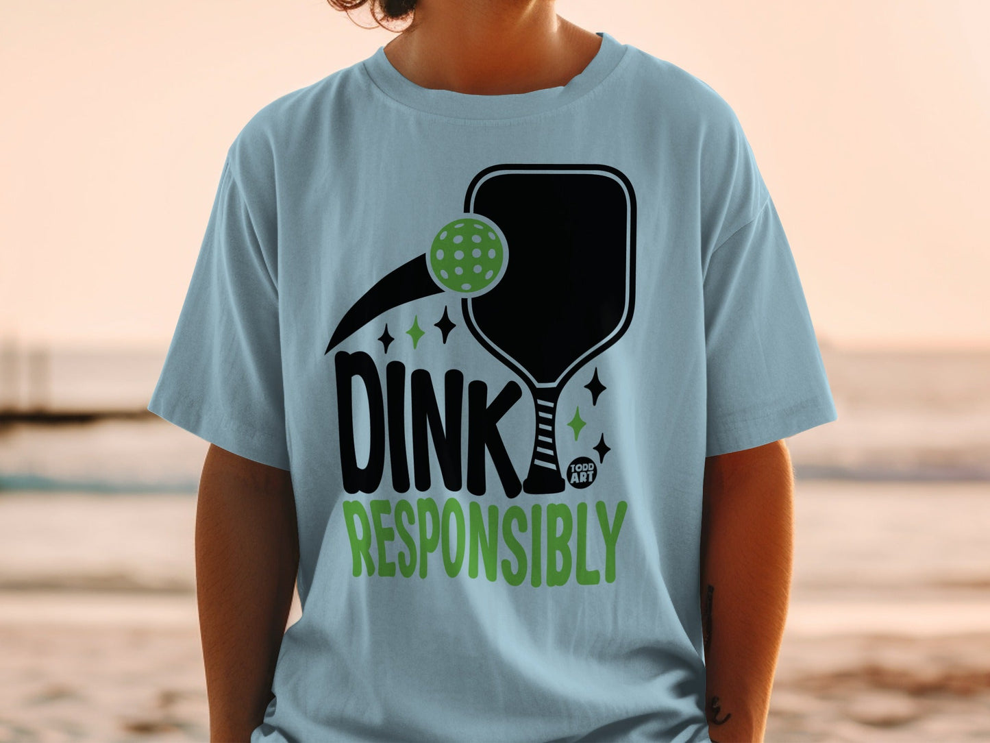 Light blue t-shirt with black pickleball graphic and "Dink Responsibly" text.