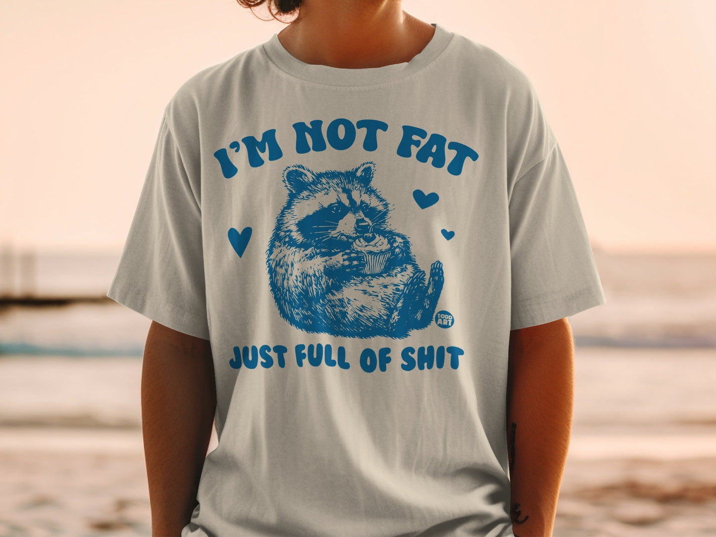 Light grey t-shirt with blue raccoon graphic and "I'M NOT FAT JUST FULL OF SHIT" text.