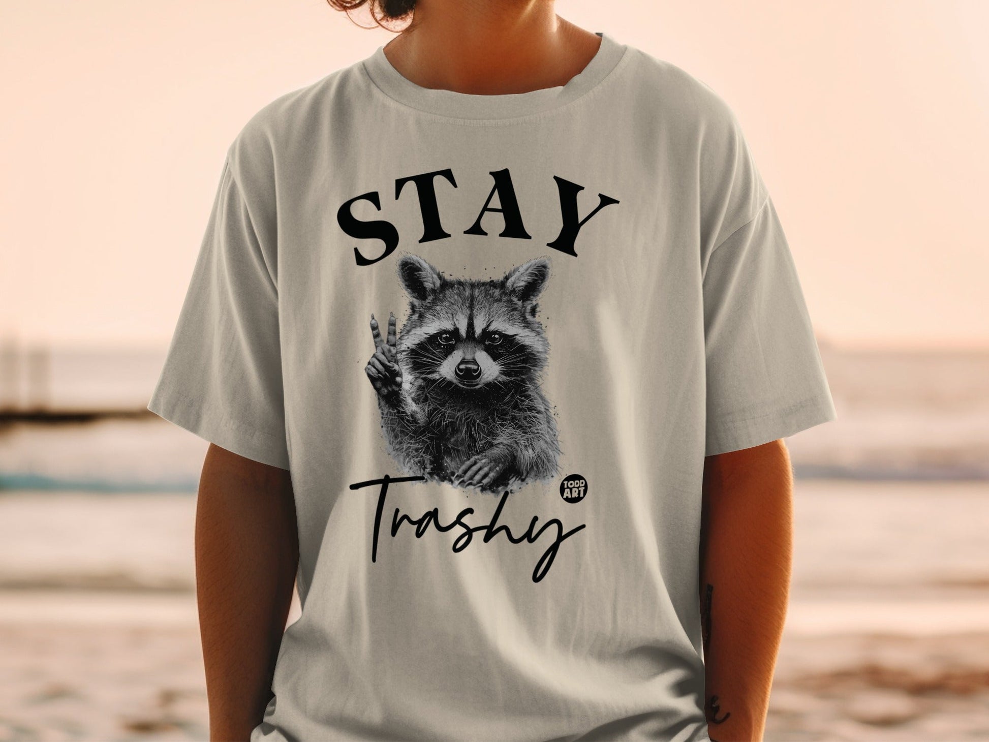 T-shirt with raccoon giving peace sign, "STAY Trashy" text.