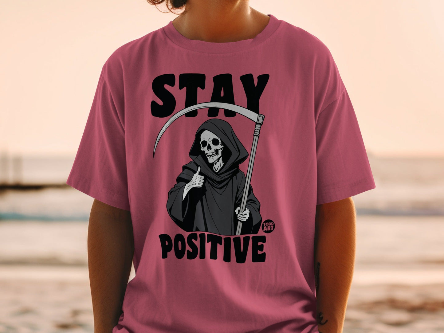 Pink t-shirt with grim reaper graphic and "STAY POSITIVE" text.
