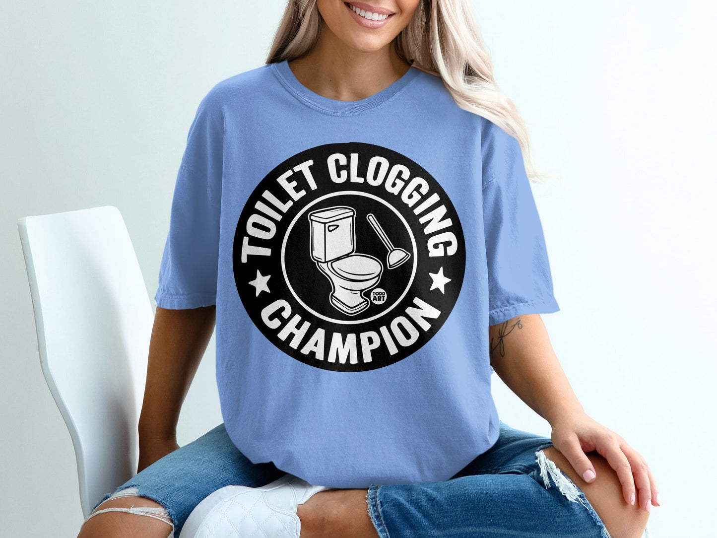 Light blue t-shirt with "Toilet Clogging Champion" text and toilet plunger graphic.