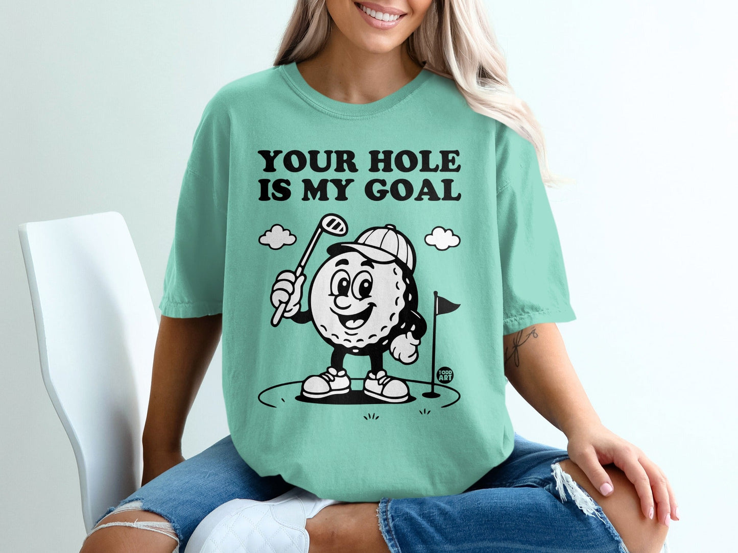 T-shirt with cartoon golf ball character and text "YOUR HOLE IS MY GOAL".