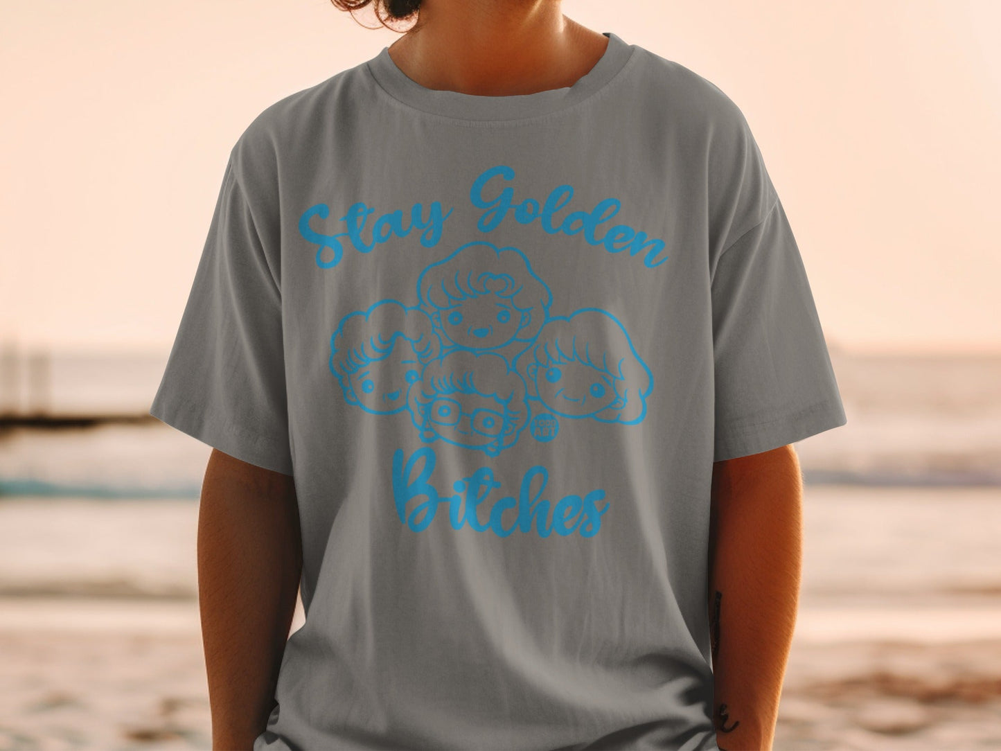 Grey t-shirt with "Stay Golden Bitches" and four cartoon faces in blue.