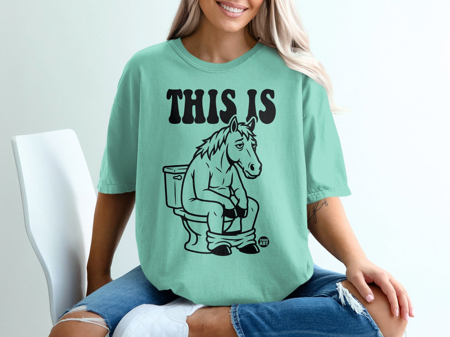 Teal t-shirt with a horse sitting on a toilet, text reads "THIS IS".