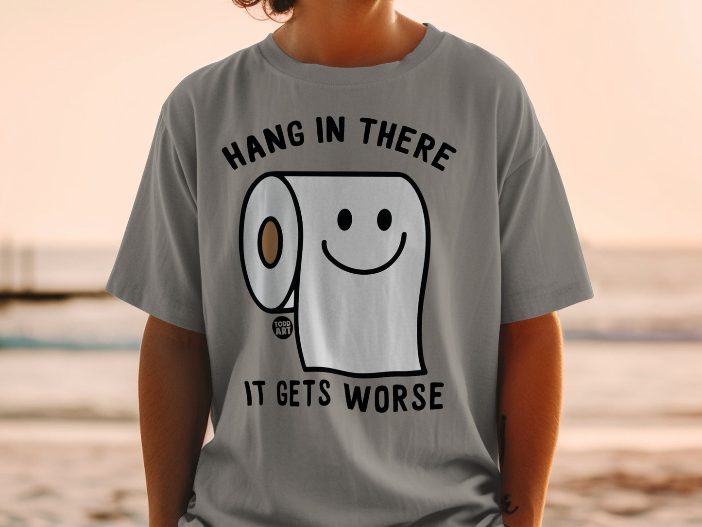 T-shirt with toilet paper roll and smiley face, "Hang in there. It gets worse." text.