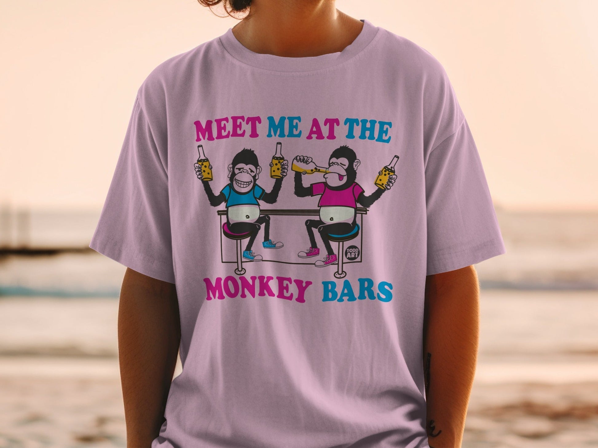 Pink t-shirt with cartoon monkeys at a bar holding bottles.
