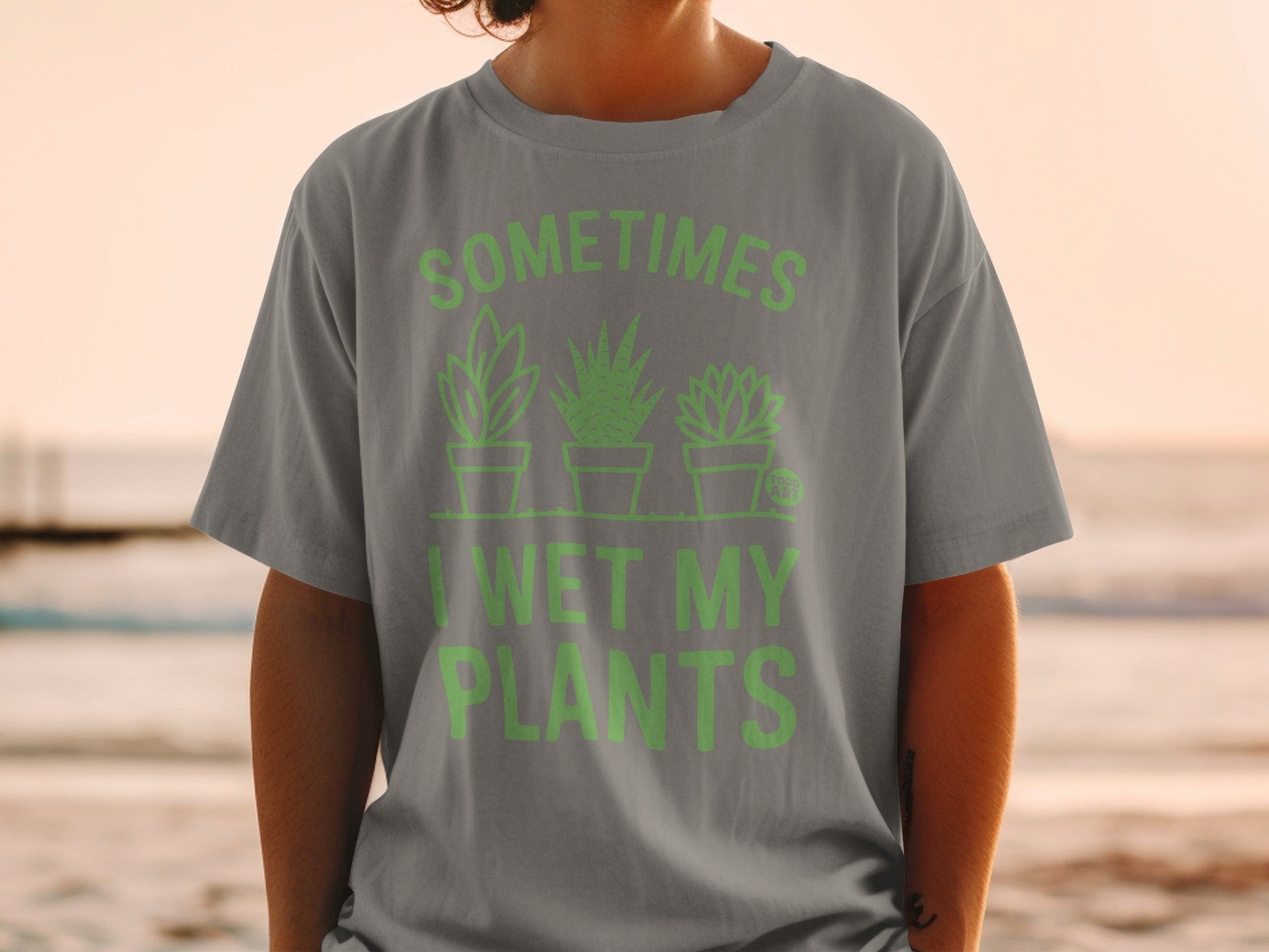 Grey t-shirt with light green text "SOMETIMES I WET MY PLANTS" and plant illustrations.