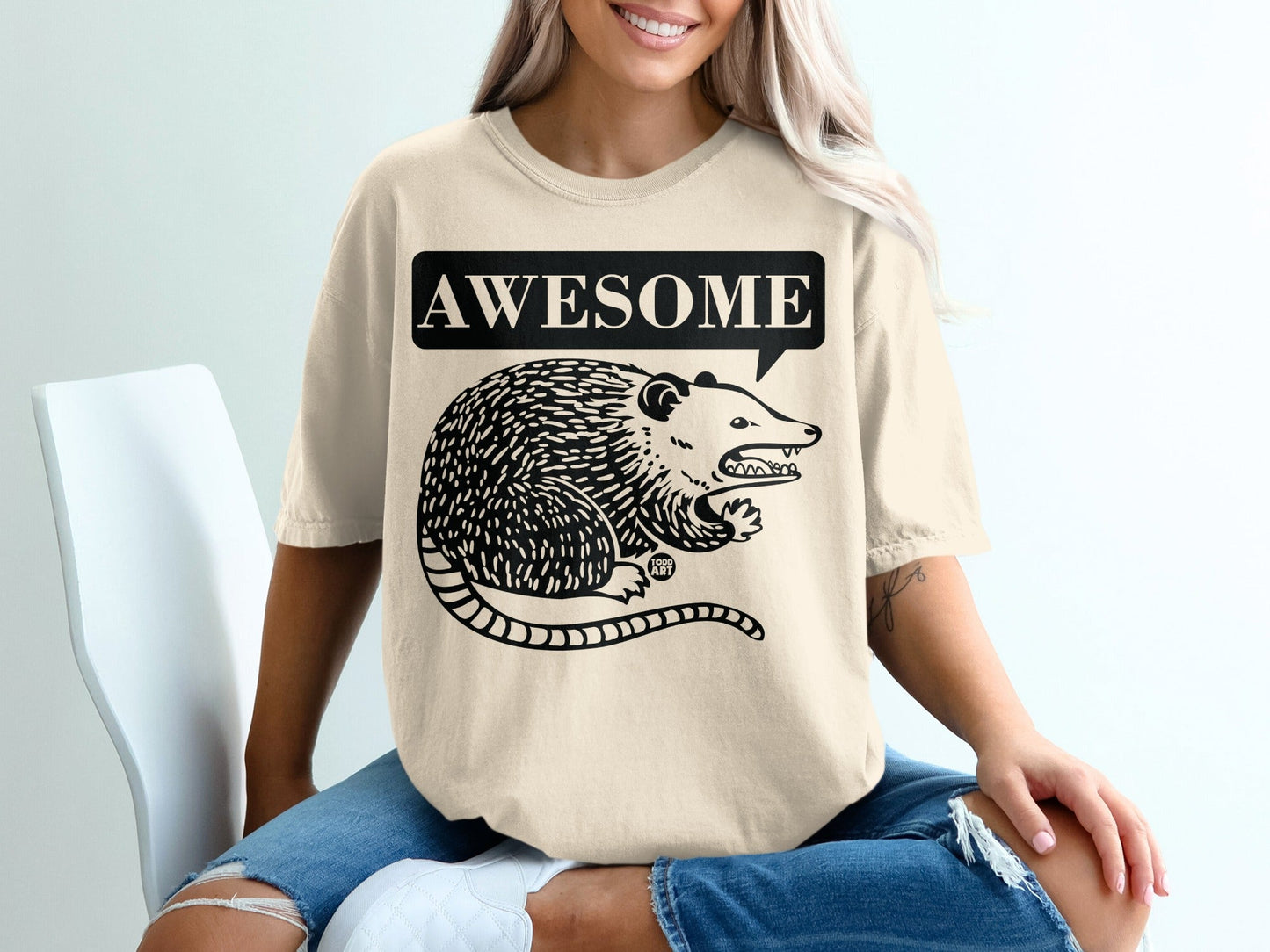 Beige t-shirt with a black illustration of a possum and the word "AWESOME" in a speech bubble.