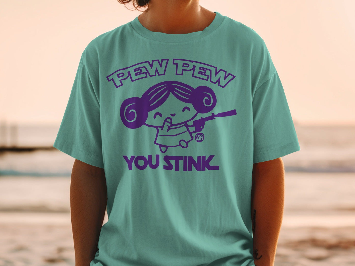 Teal t-shirt with purple graphic "Pew Pew You Stink" and cartoon girl with blaster.