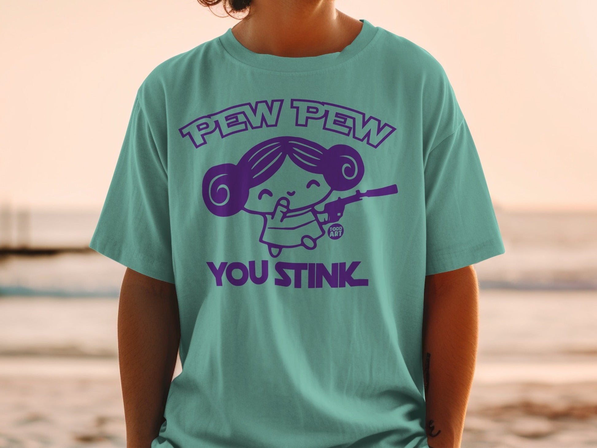 Teal t-shirt with purple graphic "Pew Pew You Stink" and cartoon girl with blaster.