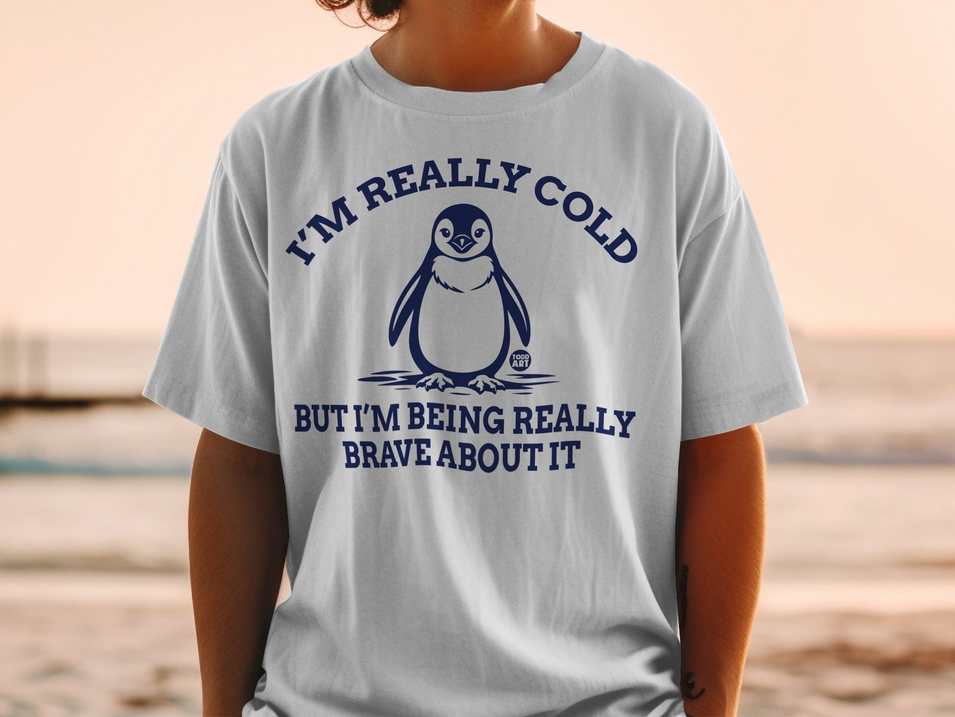 White t-shirt with penguin illustration and "I'M REALLY COLD BUT I'M BEING REALLY BRAVE ABOUT IT" text.