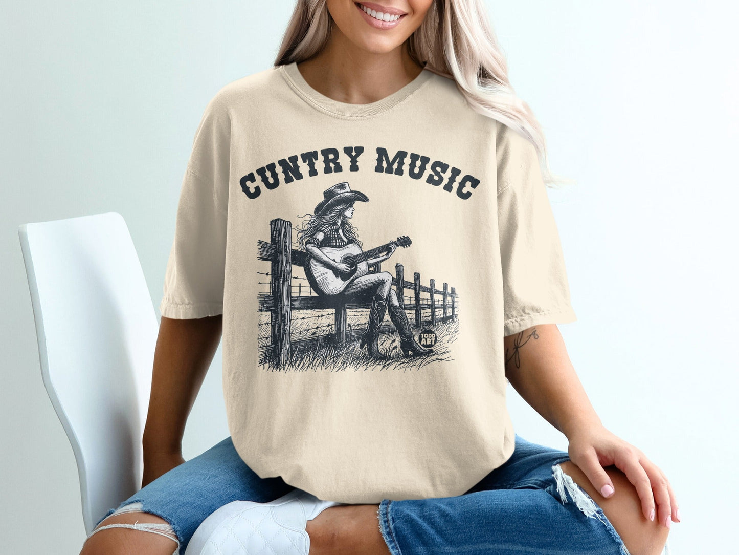 T-shirt with "CUNTry Music" text and illustration of a woman playing guitar on a fence.
