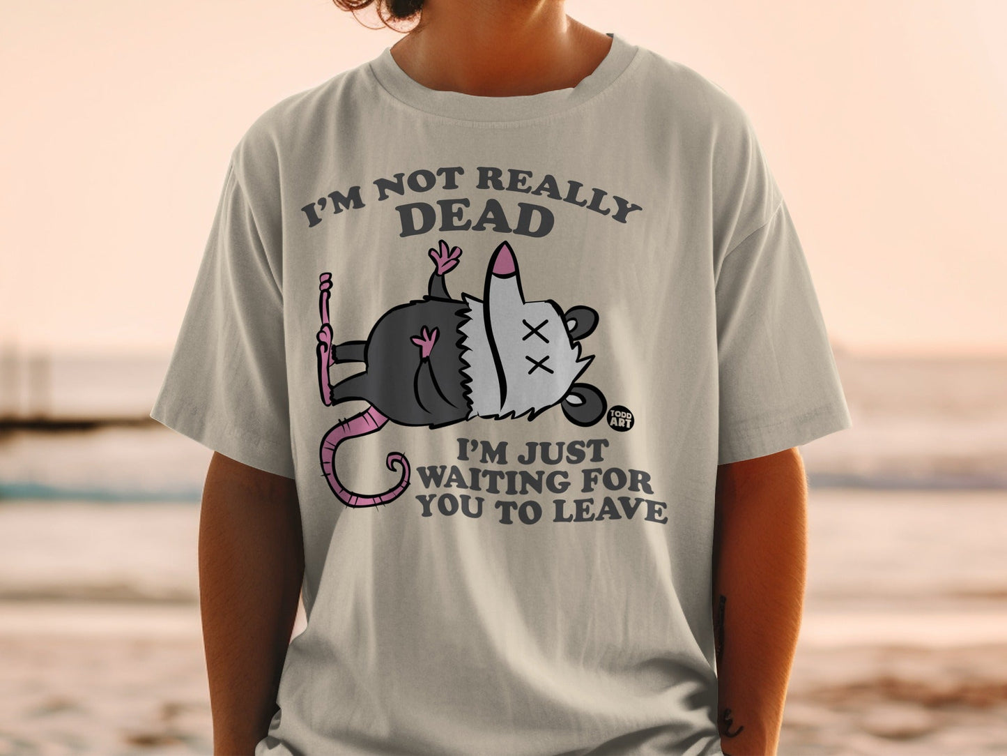 T-shirt with cartoon possum playing dead, text reads "I'm not really dead, I'm just waiting for you to leave."