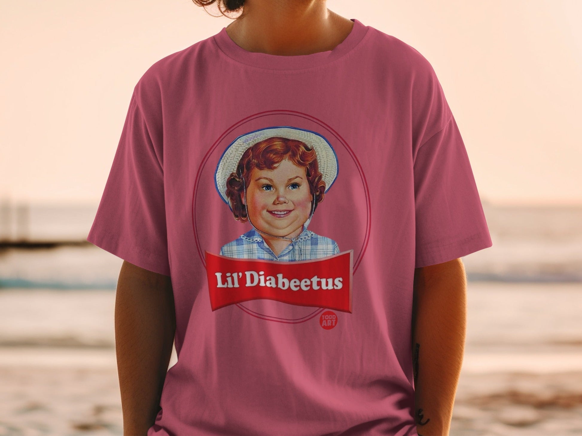 Pink t-shirt with a Lil' Diabeetus cartoon girl in a hat and blue plaid shirt.