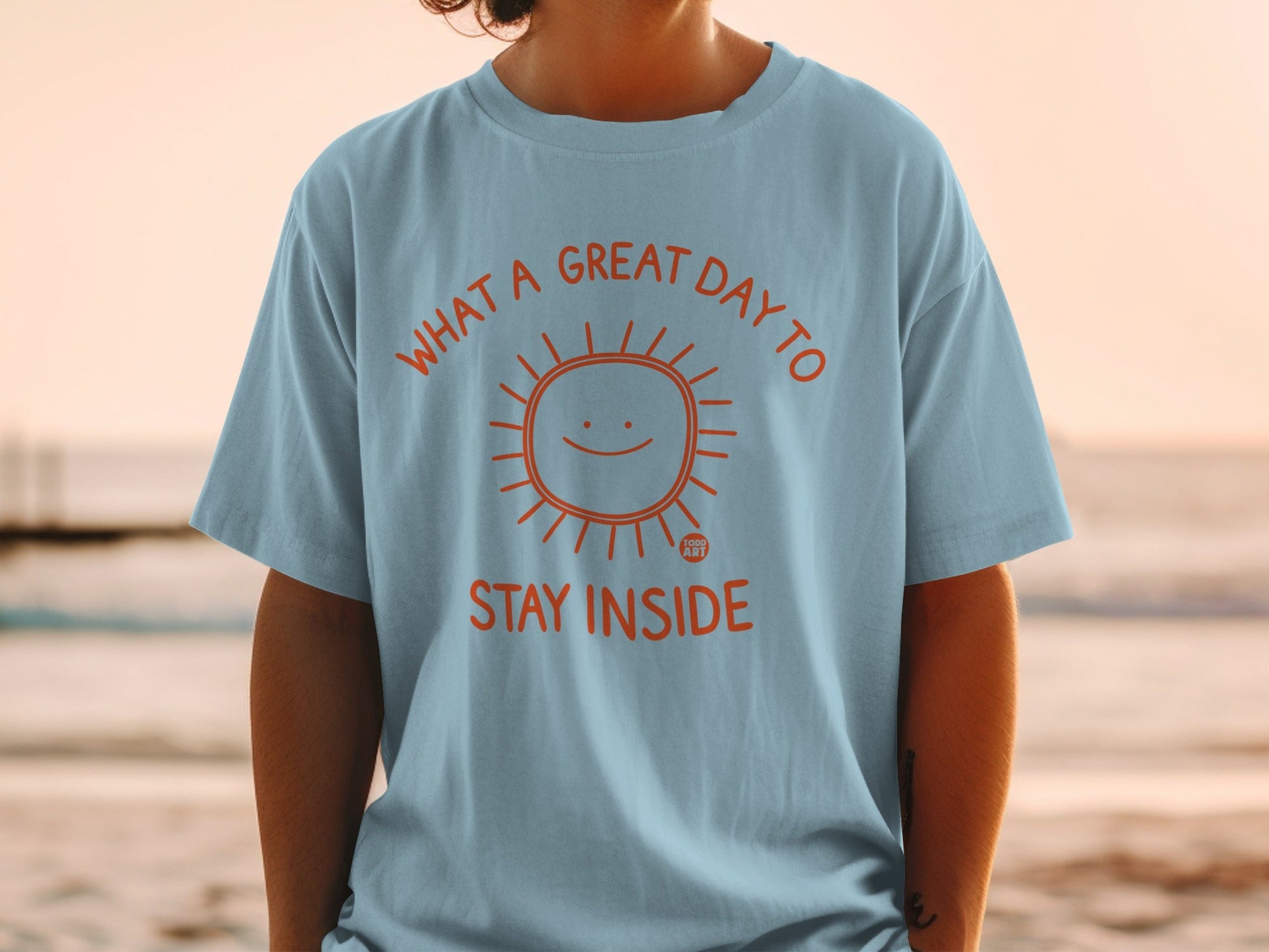 Light blue t-shirt with orange sun graphic and "What a great day to stay inside" text.