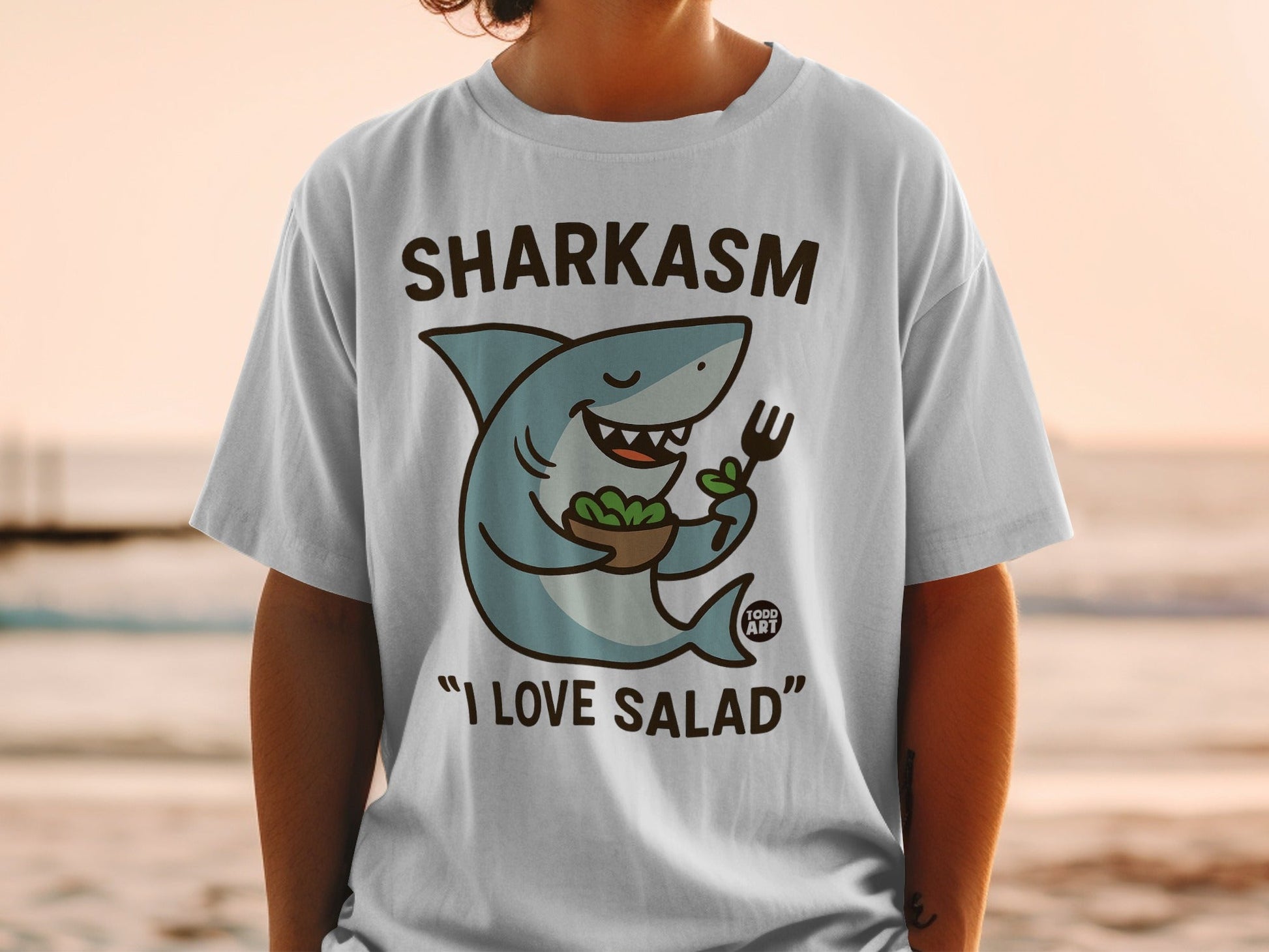 T-shirt with a cartoon shark holding a fork and salad, reading "Sharkasm I Love Salad".