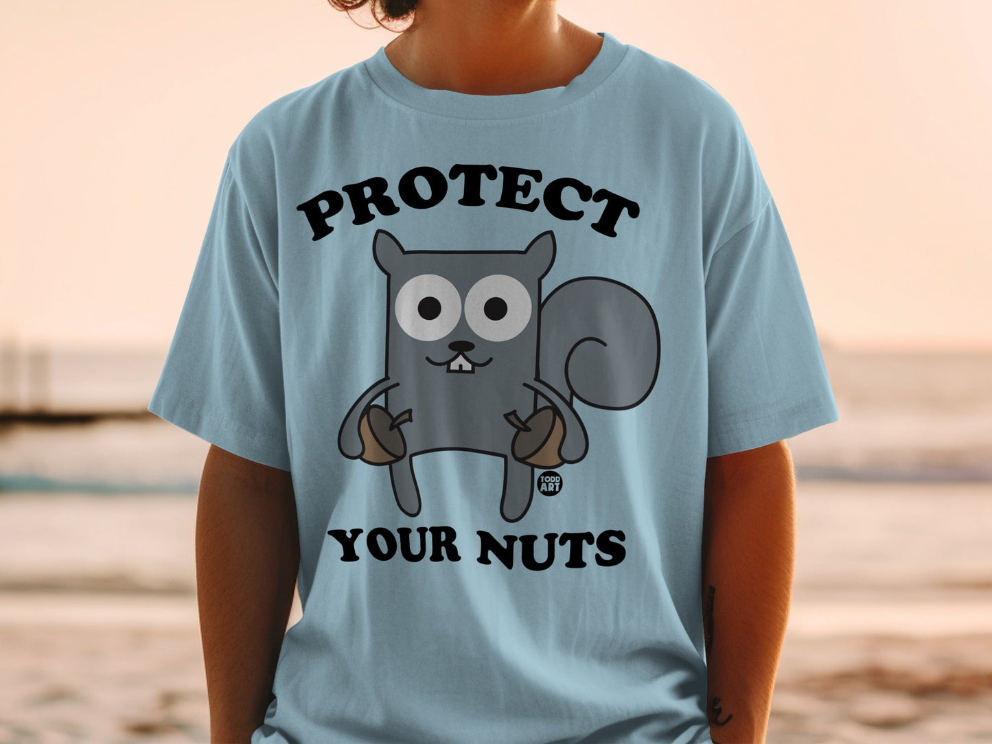 Light blue t-shirt with a cartoon squirrel holding acorns and text "PROTECT YOUR NUTS".