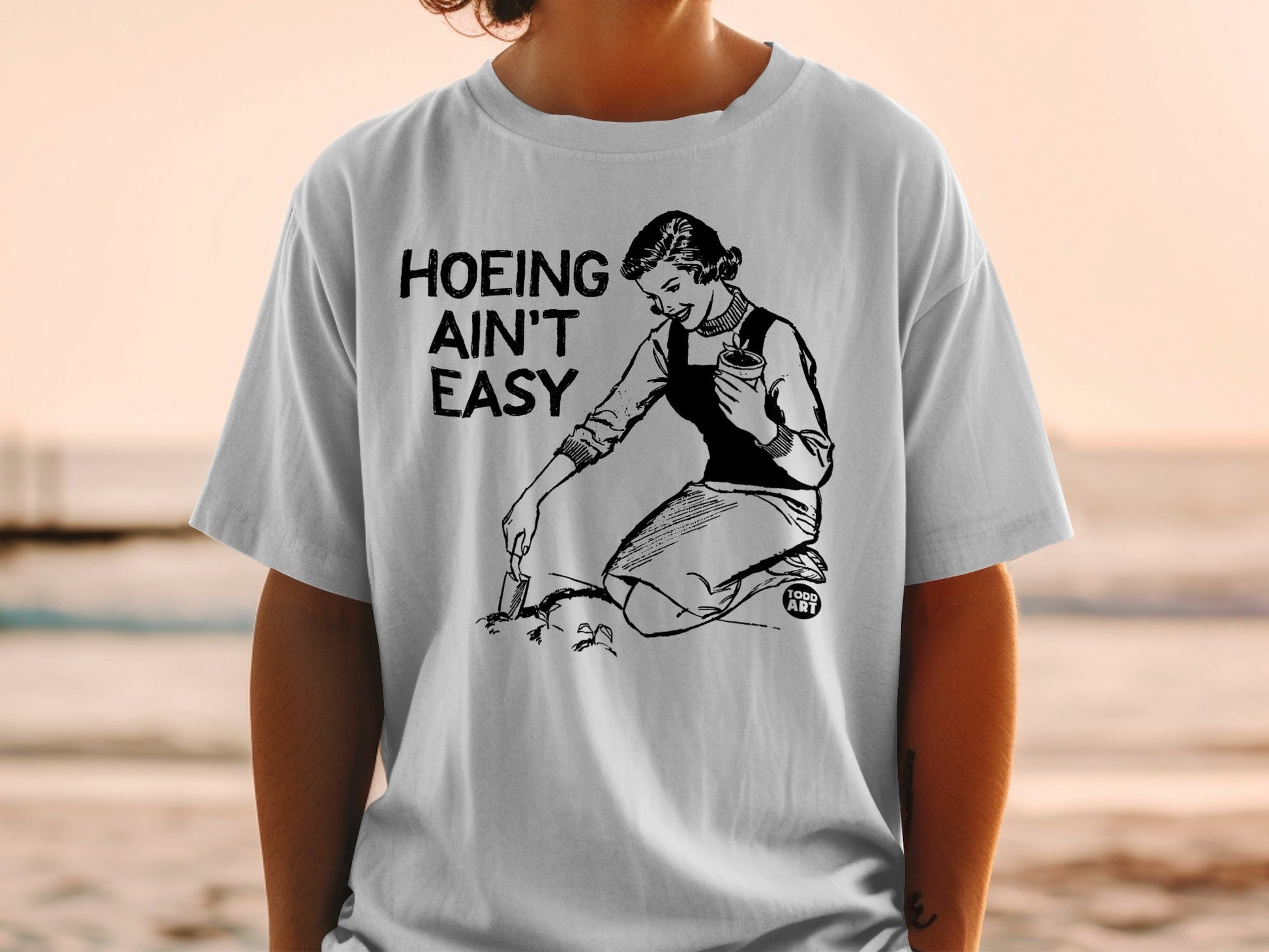 T-shirt with woman gardening and text "Hoeing Ain't Easy".