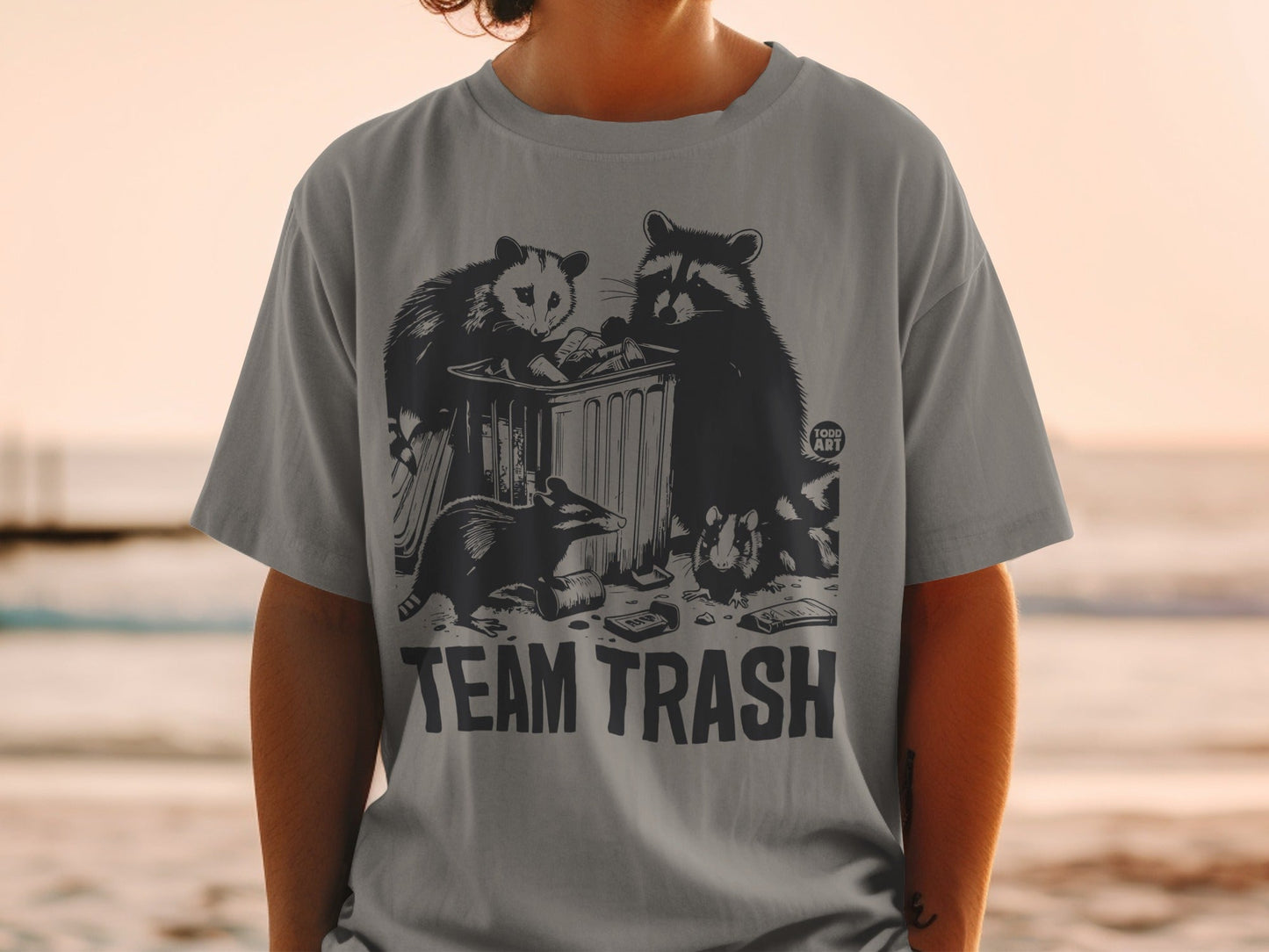 Gray t-shirt with "TEAM TRASH" and raccoons and opossums digging in a trash can.
