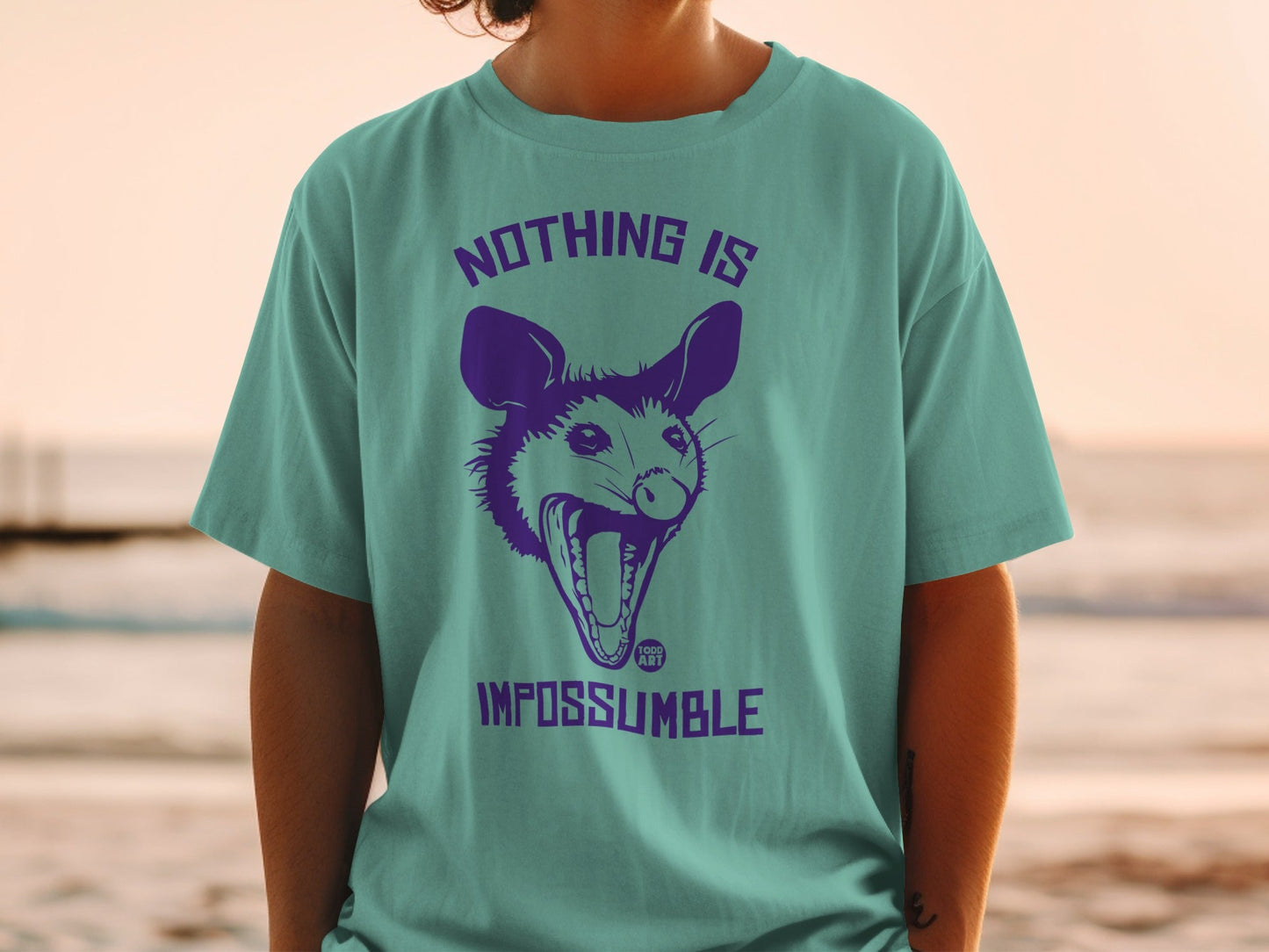 Teal t-shirt with a purple graphic of a screaming possum and text "NOTHING IS IMPOSSUMBLE".
