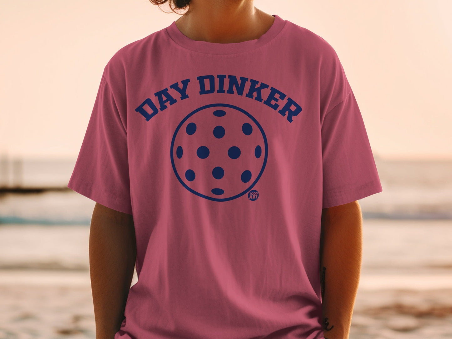 Pink t-shirt with blue "DAY DINKER" text and pickleball graphic.