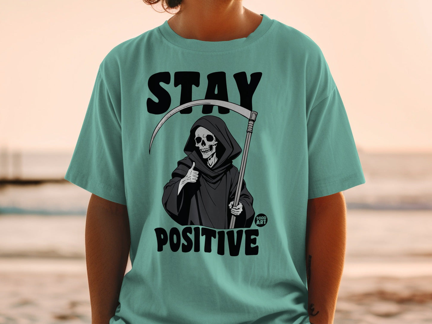 T-shirt featuring a grim reaper character giving a thumbs up with "STAY POSITIVE" text.