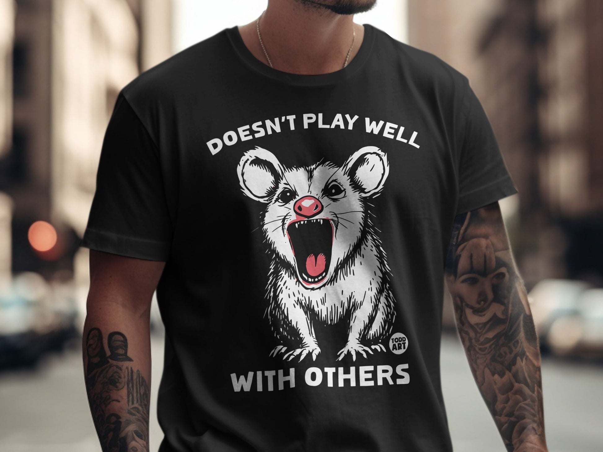 Black t-shirt with a screaming opossum graphic and text "DOESN'T PLAY WELL WITH OTHERS".