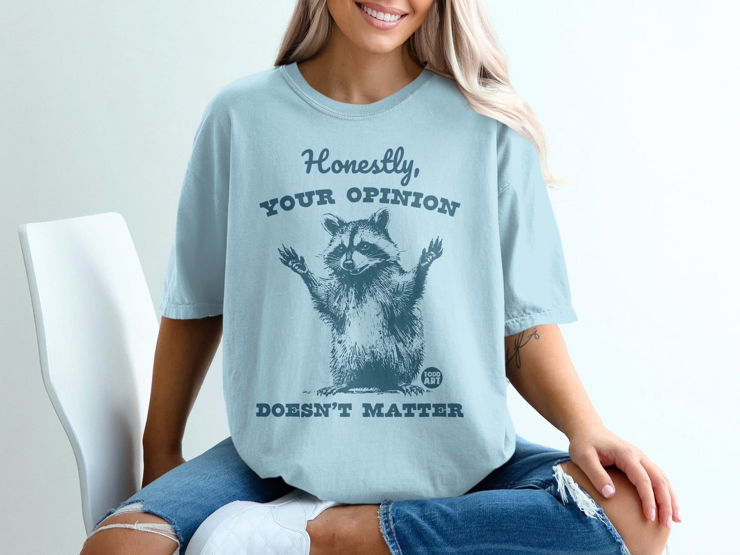 Light blue t-shirt with raccoon graphic and text "HONESTLY, YOUR OPINION DOESN'T MATTER."