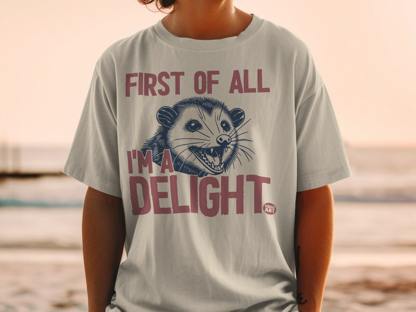 T-shirt with a possum graphic and "First of all, I'm a delight" text.