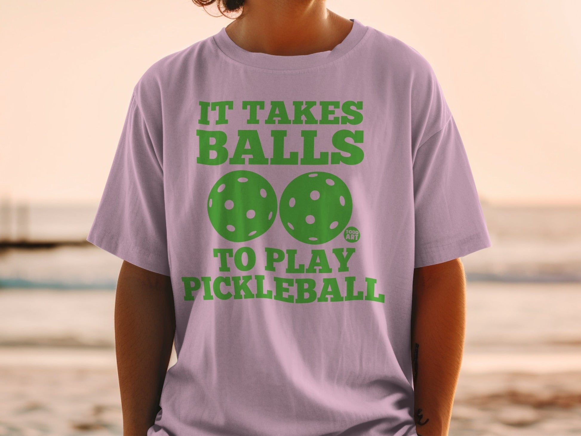 Purple t-shirt with green text and pickleballs reading "IT TAKES BALLS TO PLAY PICKLEBALL".