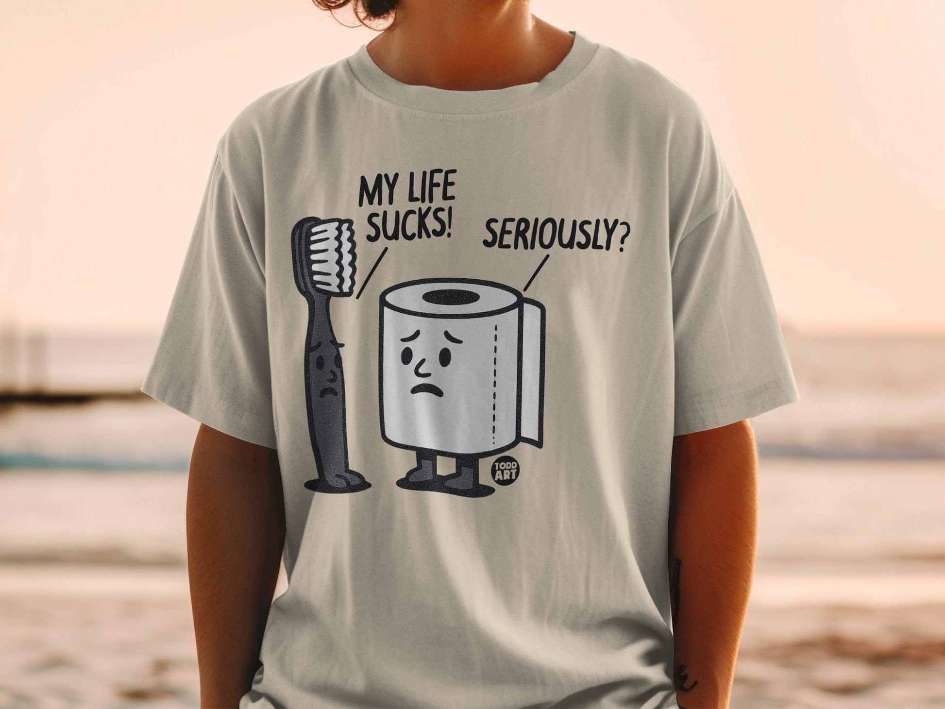 T-shirt with cartoon toilet paper and toothbrush characters saying "My life sucks! Seriously?".