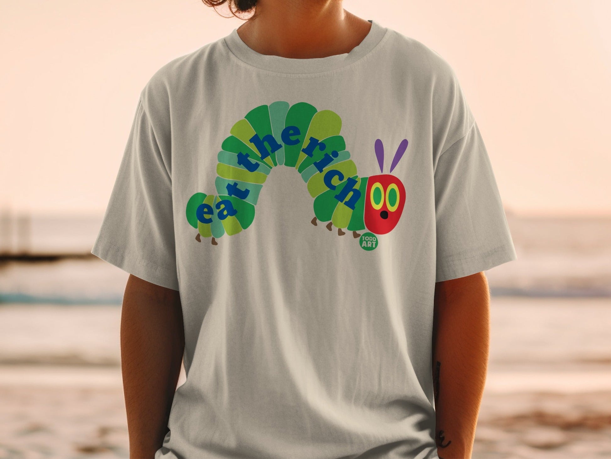 T-shirt featuring "the very hungry caterpillar" eating with "eat the rich" text.